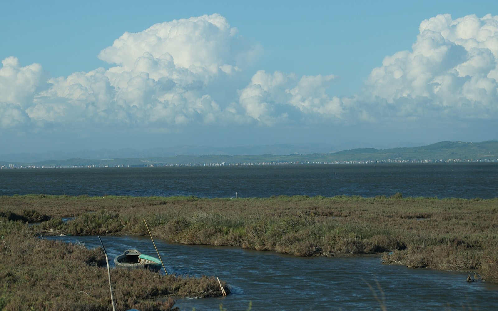 A shallow lagoon fringed with marsh grass, a small boat drawn up, tall clouds behind