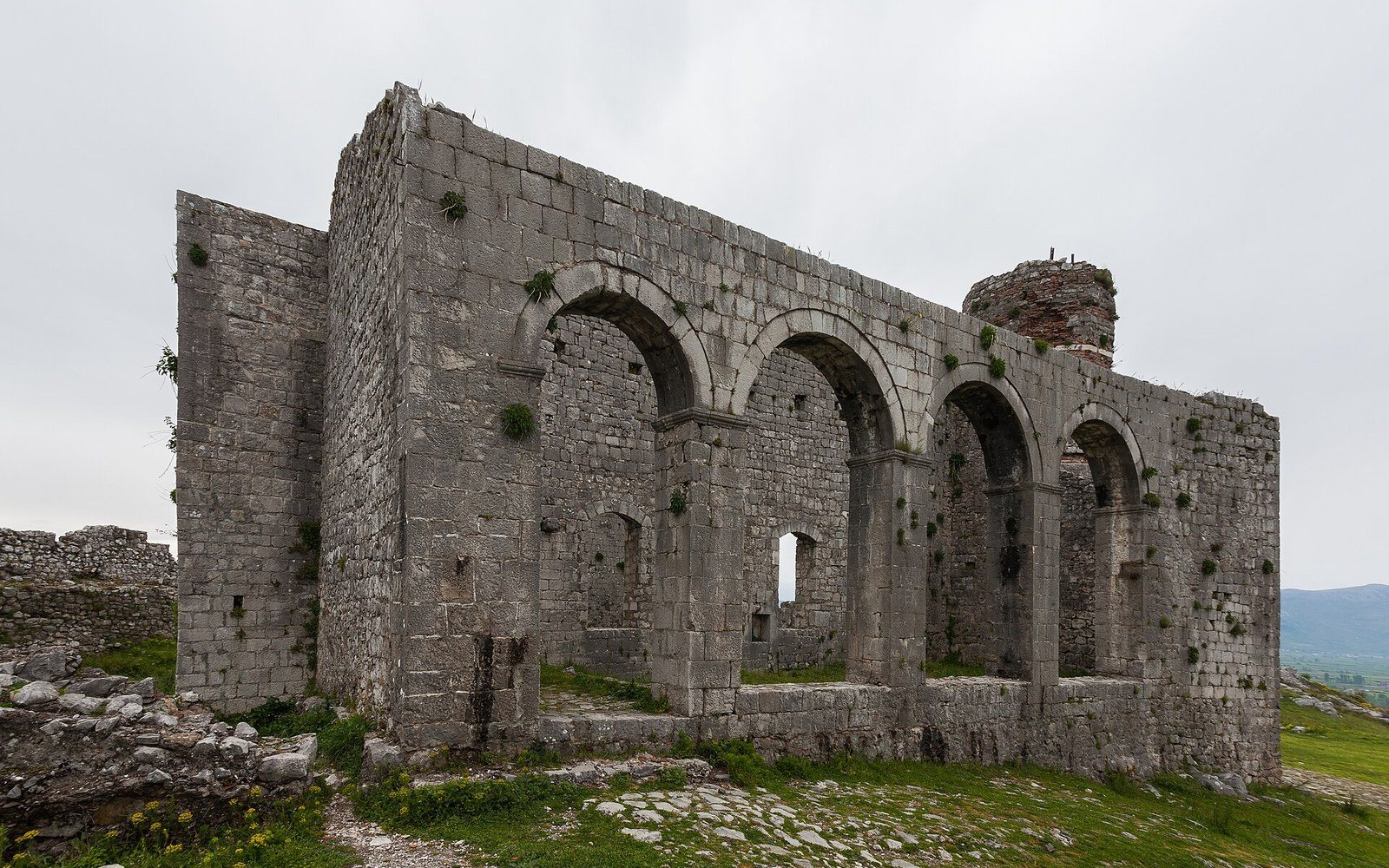 A roofless stone church of four arched bays inside a castle enclosure